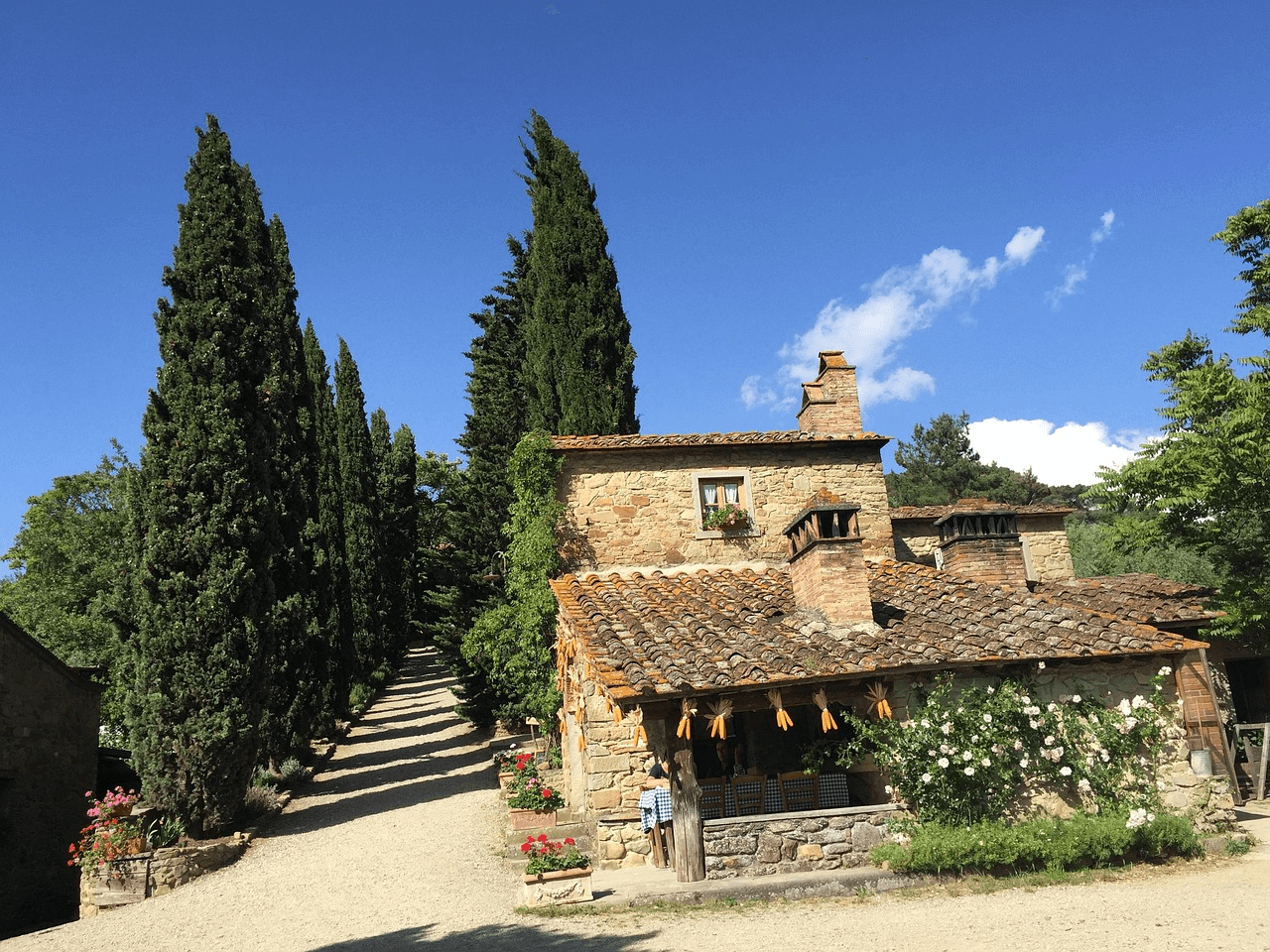 Aldeias Secretas da Toscana: Casa de pedra tradicional da Toscana com ciprestes altos e caminho de cascalho, representando o charme de uma aldeia secreta na região.
