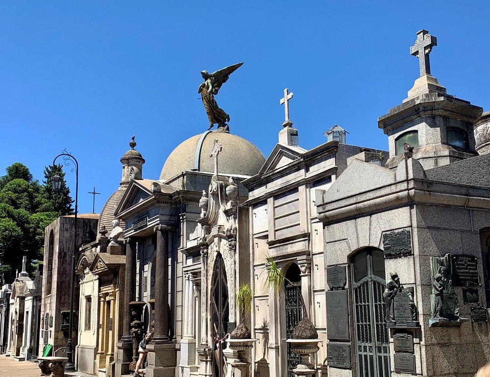 Túmulos elaborados e esculturas artísticas no Cemitério da Recoleta, em Buenos Aires, sob um céu azul claro.