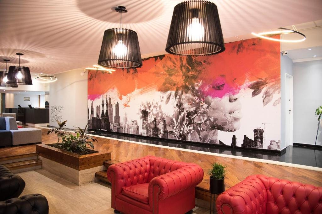 Área de recepção moderna e artística do hotel CLH Rentals em Buenos Aires, com poltronas vermelhas e mural colorido ao fundo.