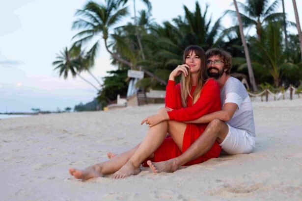 lua de mel em zanzibar praias: Casal romântico em lua de mel sentado na areia branca da praia de Zanzibar ao entardecer, mulher de vestido vermelho e homem abraçados com palmeiras tropicais e oceano cristalino ao fundo